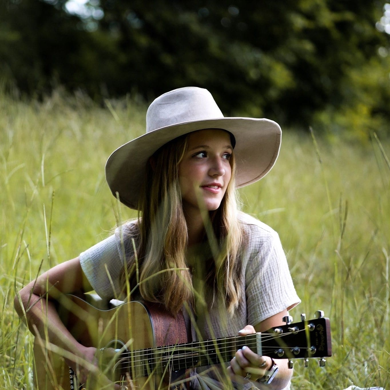 Anslee Davidson holding a guitar sitting in a field